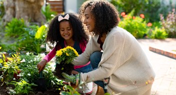 Spring Maintenance Happy african american mother and daughter planting flowers. family time, having fun together at home and garden.