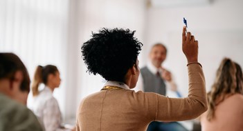 Resources for Multifamily Boards Back view of African American student raising her arm to answer a question during lecture in the classroom.