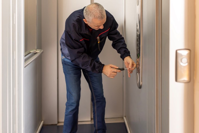 Mature engineer maintaining elevator in building. Lift machinist man repairing elevator fixing or adjusting mechanism.